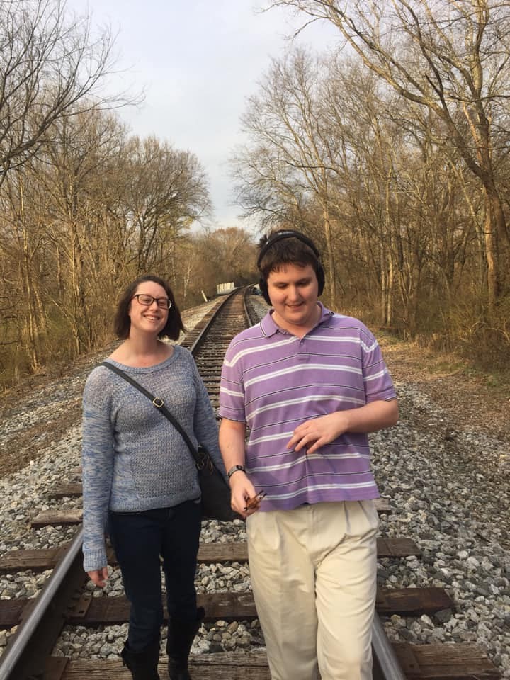Emma, a 31 year old white woman, and her younger brother Evan, a 24 year old white man, walking on a sunny day on train tracks at a local park