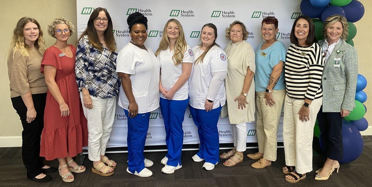 A group of 10 women post in front of a backdrop that says HH Health System
