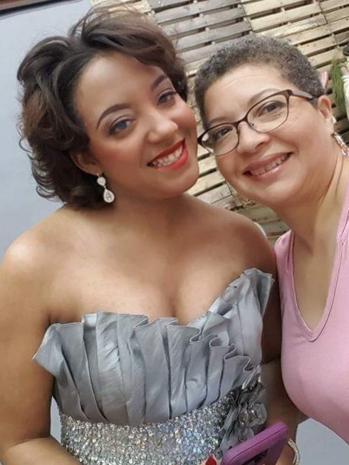Cathlyn and her daughter Tyler shows Cat and her daughter, Tyler, who is a young woman in her twenties. In this photo, Tyler has styled short curly hair, big silver earrings, and a strapless silver ruffled fancy dress – she looks like she is dressed for a formal event.