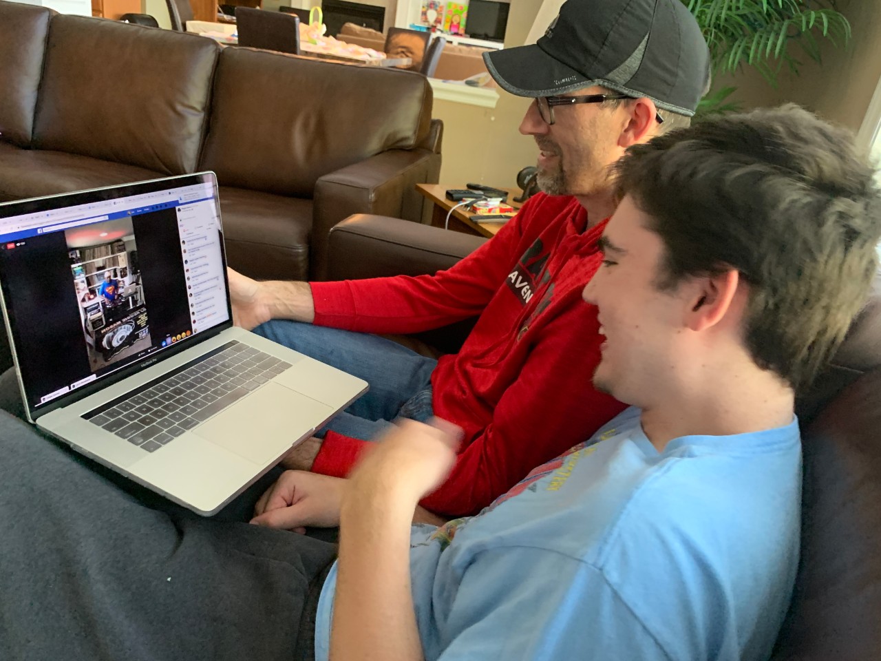 Aidan Vogus and his dad stay connected during social distancing. Aidan’s Ravenwood High Assistant Principal Reggie Mason puts on a Facebook Live DJ show each week during the quarantine to bring people together. The photo shows a young man with brown hair and a T-shirt excitedly flapping his hands, while he watches an online livestream of his school principal playing music for students. His dad sits next to Aidan, holding the laptop on his lap in their living room and smiling.