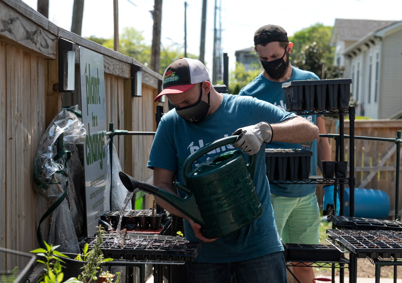 a young man wearing a Plant for a change shirt using a watering can to water plants