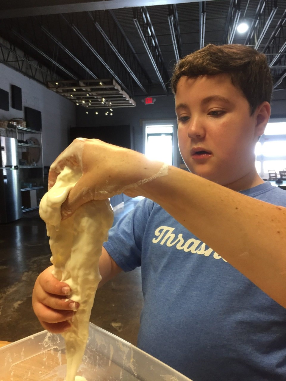Reed experiences making slime during a week of camp at DownsideUp. a young boy concentrating on holding some gooey slime over a play table.