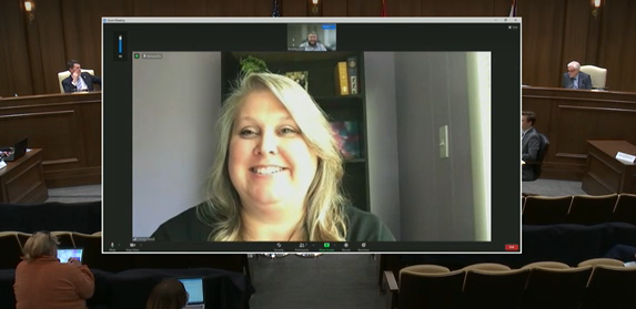 Chrissy testifying at changing tables hearing Council member Chrissy Hood – a white woman with blond hair, appears on a virtual meeting screen. Her virtual testimony is being heard in a legislative hearing room, with state legislators at the dark wood desk on the elevated dais