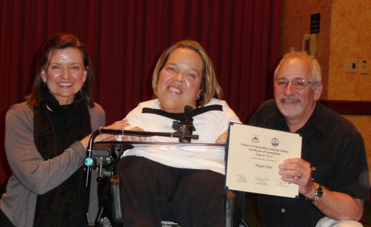 Wanda Megan Ned Partners Wanda poses on one side of Megan Hart, a woman with a physical disability who uses a wheelchair, with former Council staff Ned Solomon on Megan’s other side. Ned is holding a graduation certificate with Megan’s name.