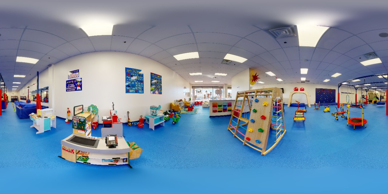 We Rock The Spectrum fish-eye lens photo showing brightly colored sensory-friendly play and gym equipment in a large gym space covered with safety mats on the floor