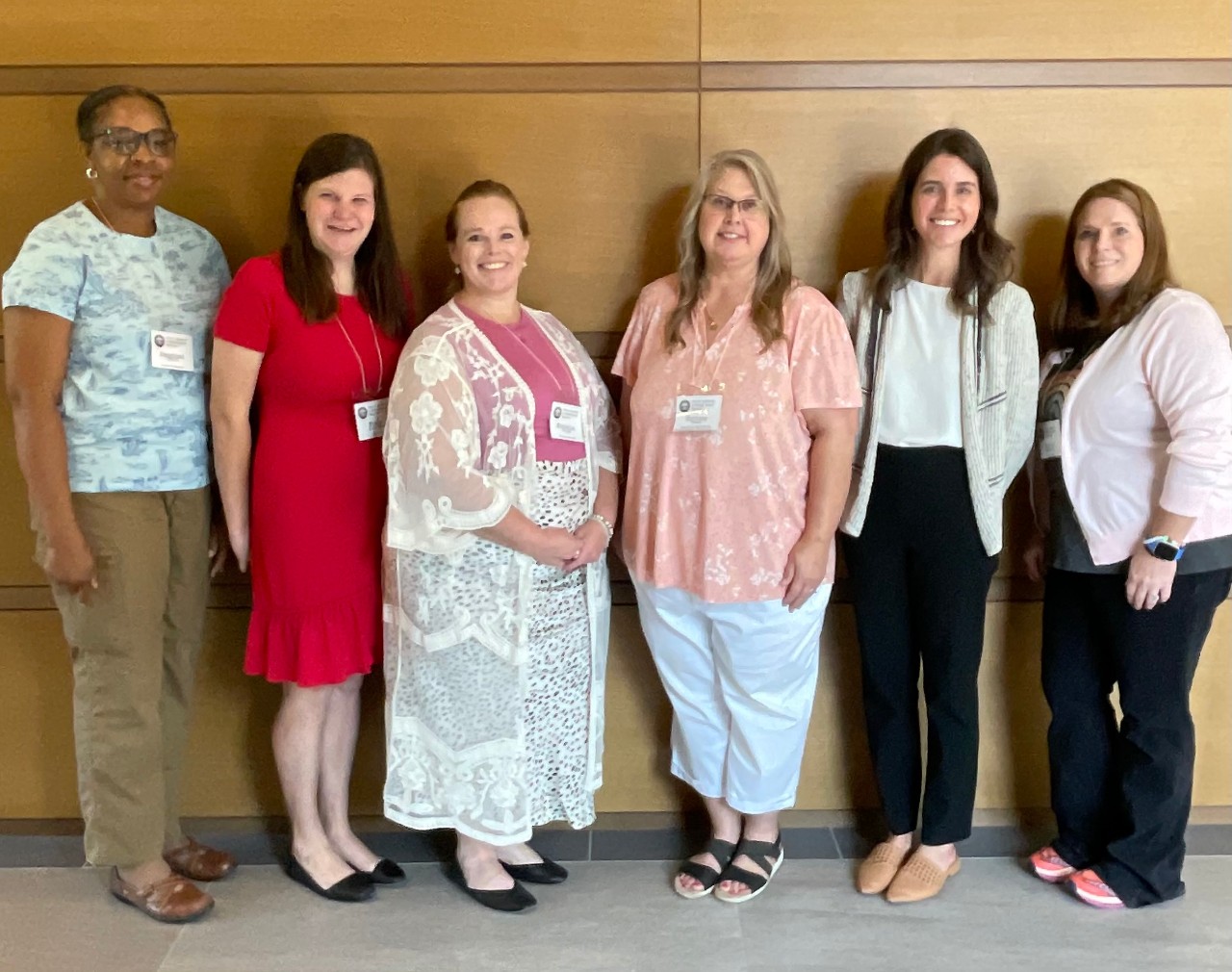 Partners grads at TDC policy retreat Six woman stand together and smile at the camera. They are wearing event badges and professional clothing.