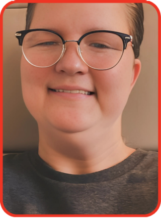 Untitled design - 1 Katie Moore, a woman with a light skin tone and short blonde hair, is smiling at the camera. She is wearing glasses and a dark-colored top, with a neutral background behind her.