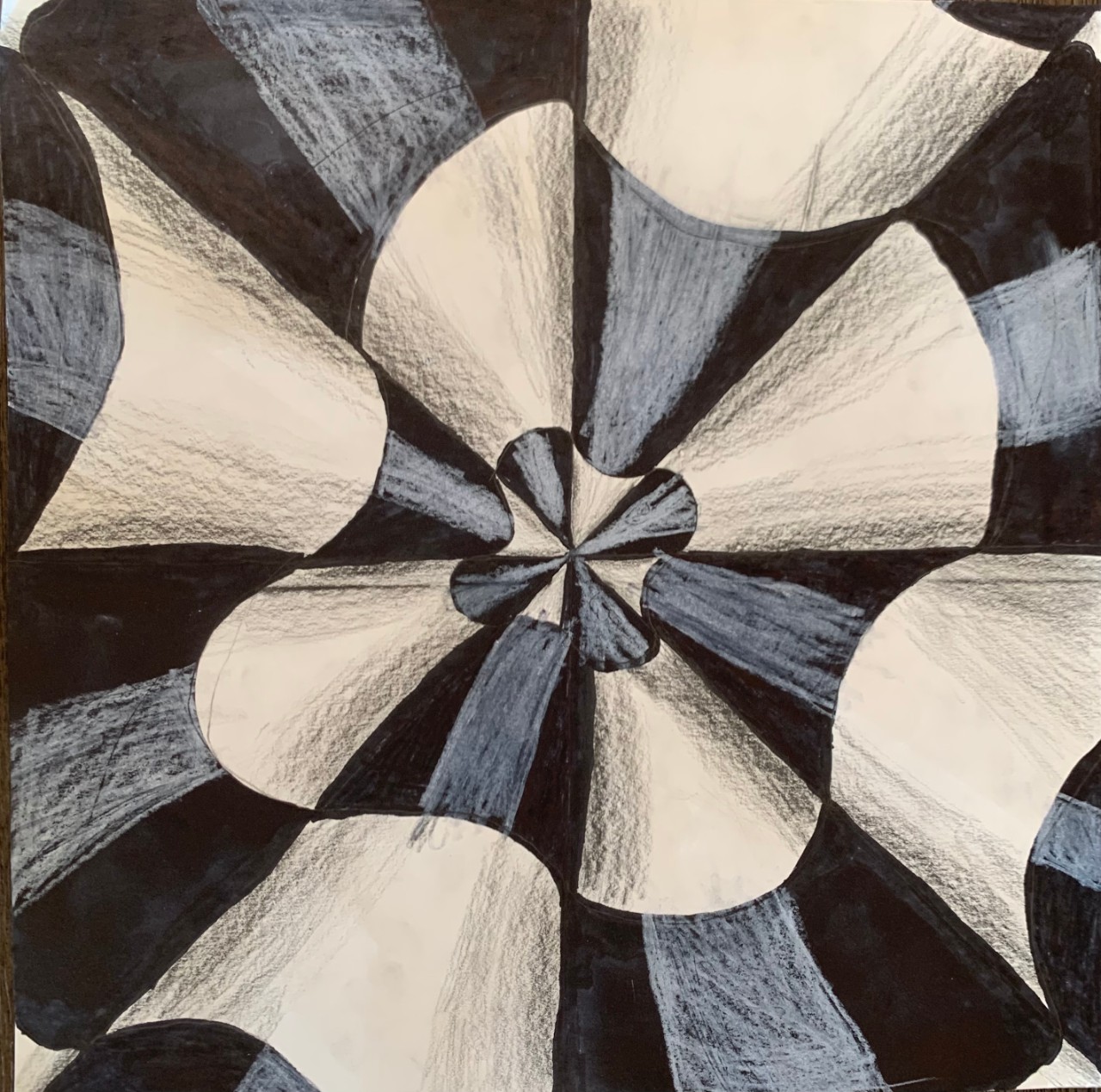 A black-and-white drawing shows a group of pencils arranged in a circular pattern, all pointing toward the center. The pencil shapes repeat and curve, creating a spinning, tunnel-like effect. Dark black sections and lighter shaded areas alternate, with visible pencil marks adding a rough, hand-drawn texture.