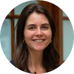 blob:https://gemini.google.com/f605ecf4-2f7b-425d-af28-b6ceb56b1900 - 1 Smiling woman with light skin and short brown hair, wearing a black blazer, pinstriped dress, and pearl necklace, standing indoors.