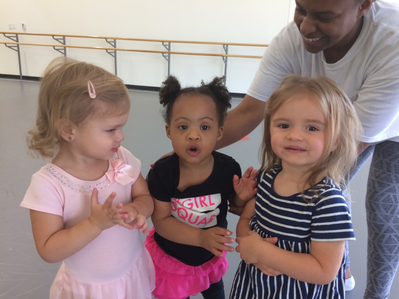 Early Childhood Inclusion Ballet class at Ballet Memphis three very young girls in their dance attire. The girl in the middle is a young girl with Down syndrome.
