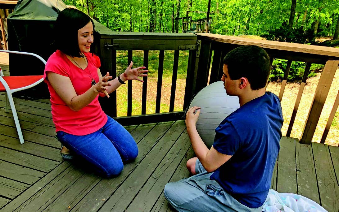 Breaking Ground 93 - Lydia and kevin sib story photo is of Lydia and Kevin, who are siblings, they are on their knees on the patio, passing a big therapy ball back and forth
