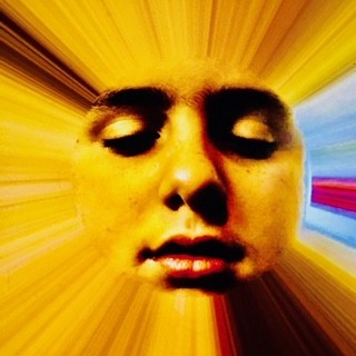a highly abstract digital photo which has a face with closed eyes in the center, with rays of gold, brown, blue and red emanating from it