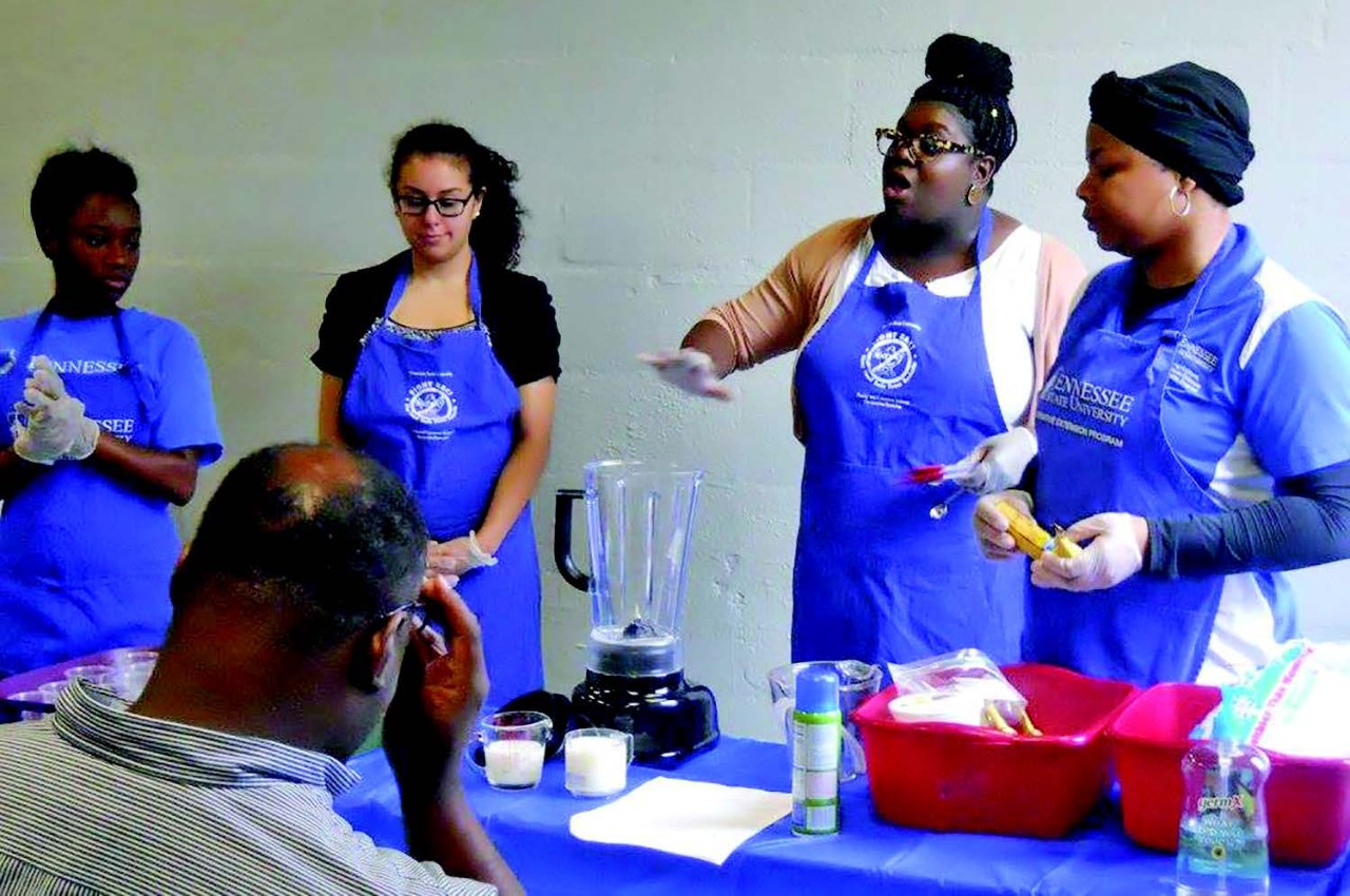 TSU Extension cooking course four TSU staff members in blue aprons are involved in a cooking class. They are from left to right: Shanail Brown (TSU SNAP-Ed PA, Davidson), Marina Fahmy (Intern, Davidson), Ebone’ Colclough (SNAP-Ed Agent, Davidson) and Latasha Holloway (EFNEP PA, Davidson).