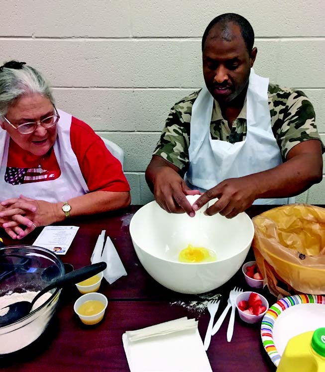 Cooking Capers class, Rutherford County, 2017 a man and a woman with aprons are working on a recipe that involves cracking an egg into a bowl