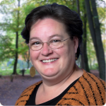 headshot of JoEllen Fowler, a white woman with short brown hair and an orange striped knit sweater and black blouse, glasses and gold earings