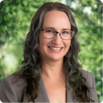headshot of Jolene Sharp, a white woman with long curly brown hair, a white blouse and a beige suit jacket