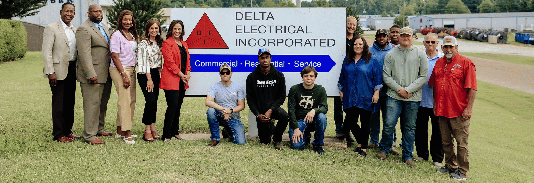 A group stands outside in front of a sign for Delta Electrical Incorporated