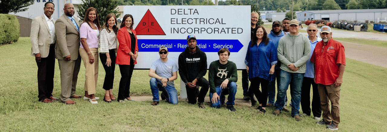 A group of 15 people stand outside in front of a sign for Delta Electrical Incorporated