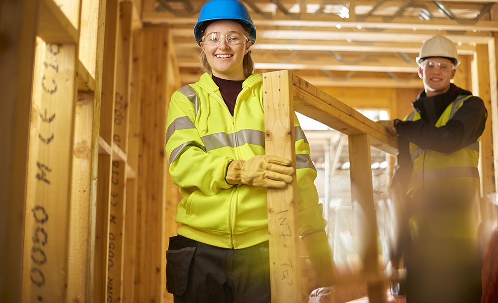 Two young people wearing safety goggles and hats on a construction site