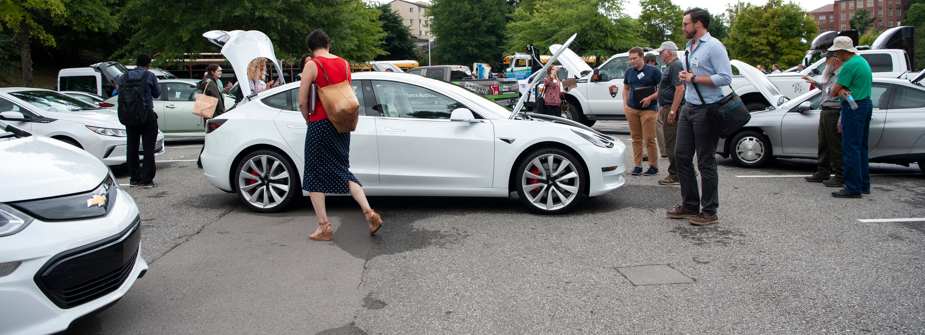 People viewing a car in a parking lot with vehicles