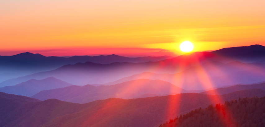 Orange and red sunset descending behind smoky mountains