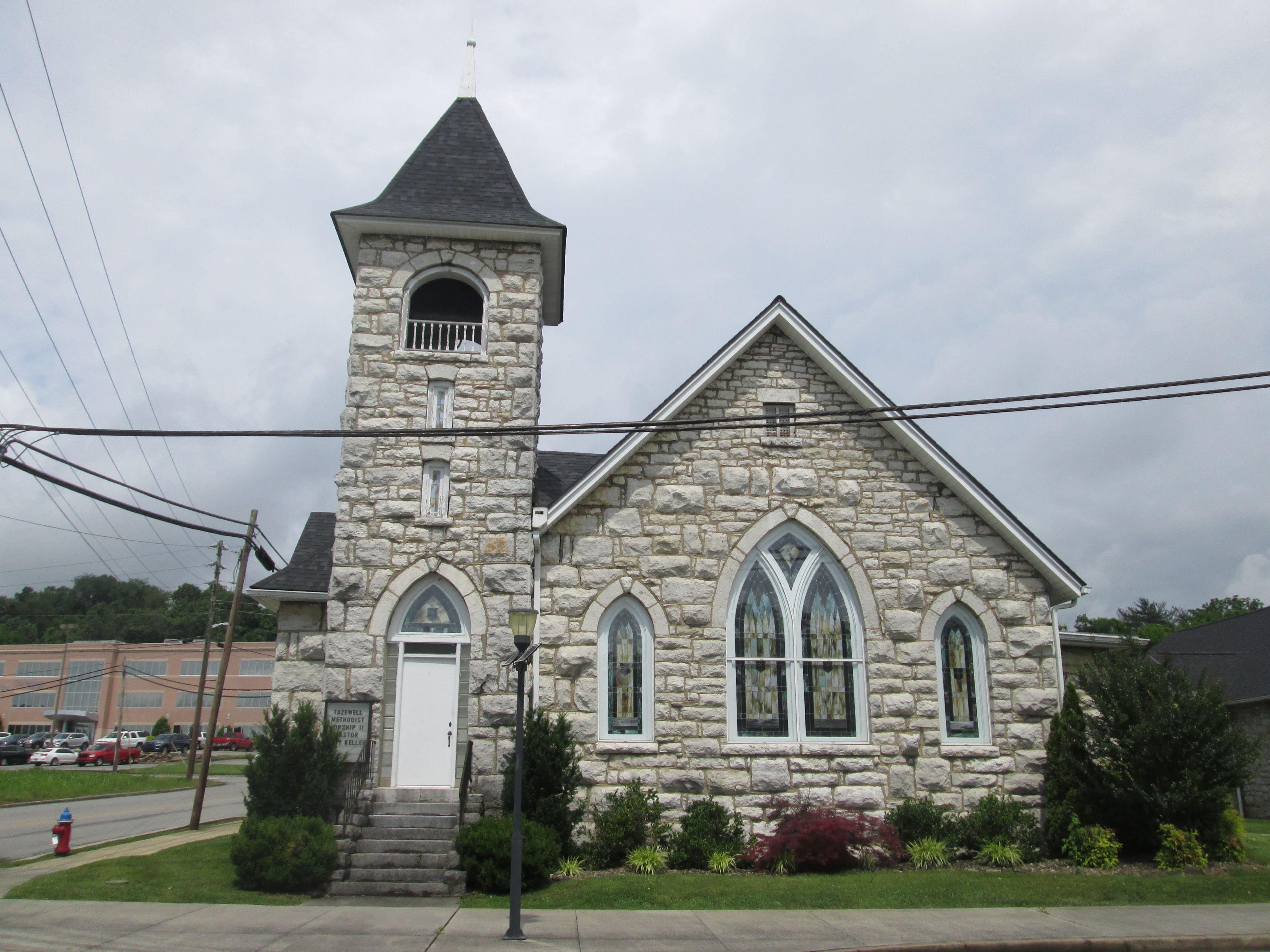 Methodist Episcopal Church South at Tazewell, a small, stone church building with a church tower and arched stained glass windows. It sits on a landscape corner lot at the intersection of two roads. 