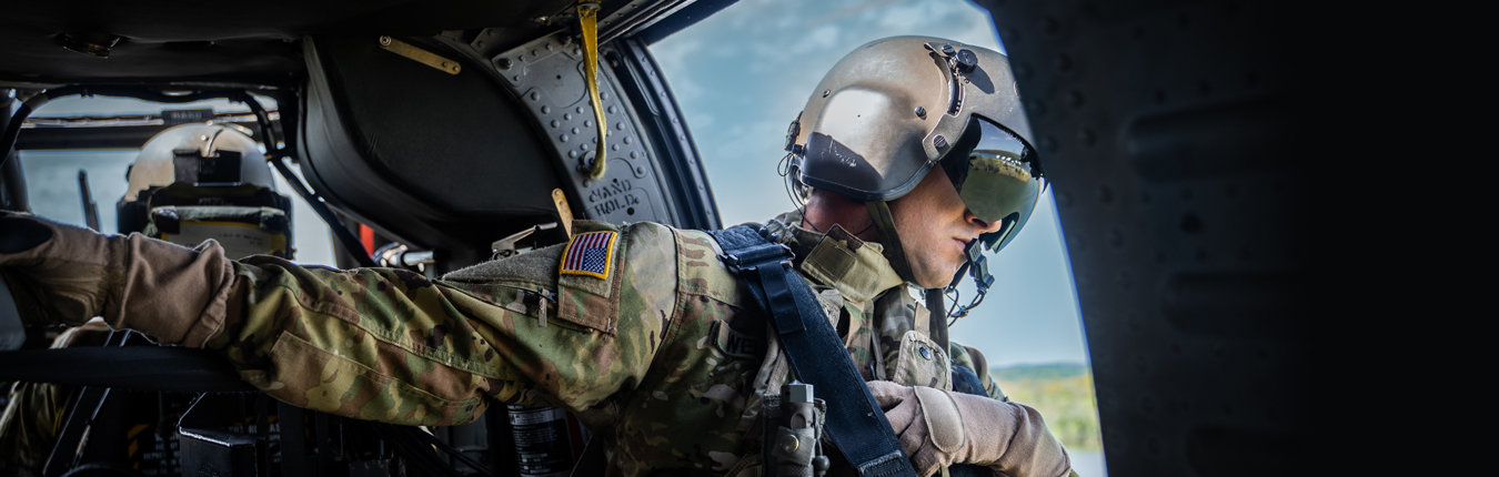 Soldier in gear and helmet leaning out of a helicopter