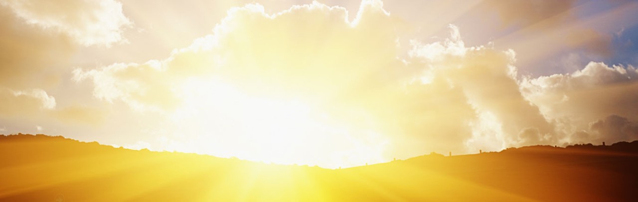 An outdoor landscape as the sun rises over the hillside brightly shining through the clouds.