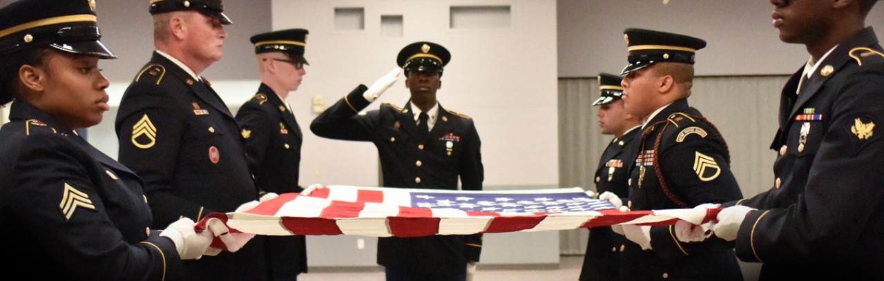 Military personnel in dress uniforms preparing to fold an American Flag during a funeral honors ceremony.