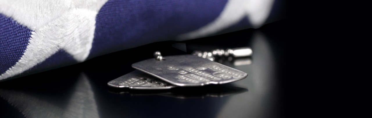 Soldier dogtags lay on a black table next to a folded American Flag.