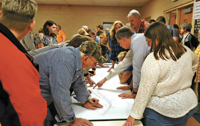 Several people stand around a table writing on paper.