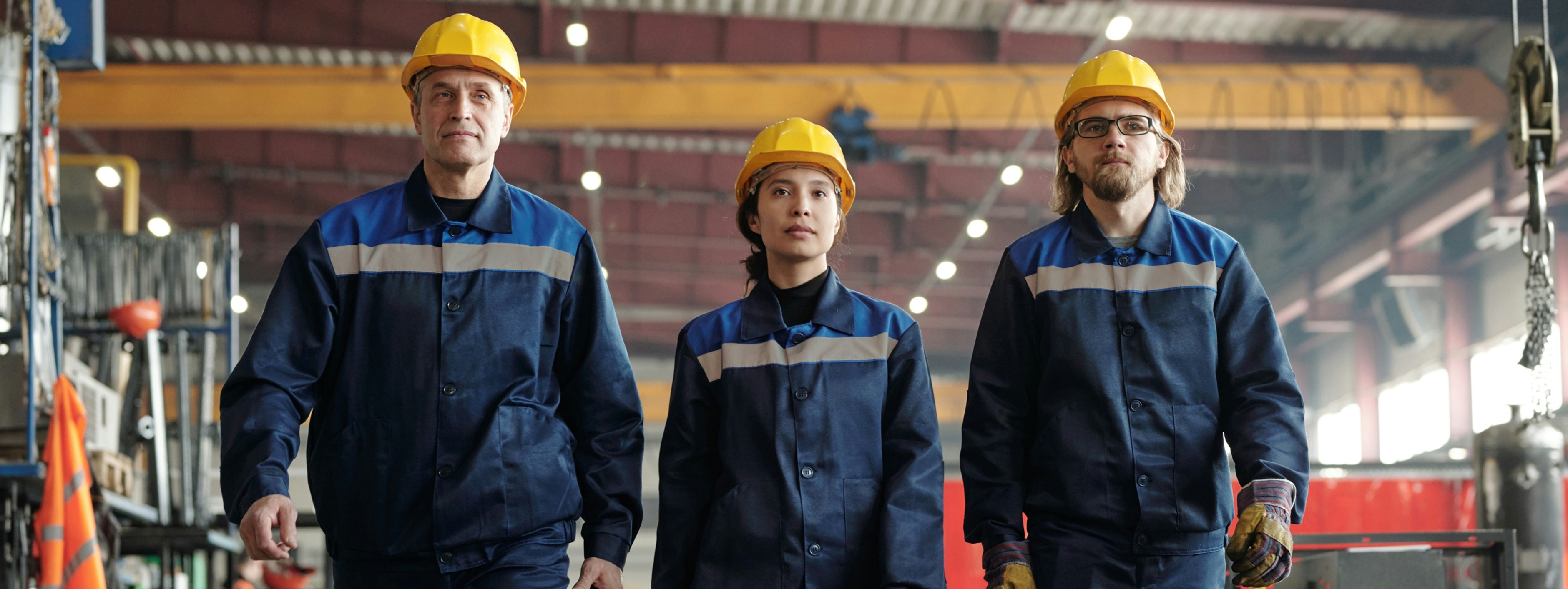 3 workers in yellow hardhats walking through a factory