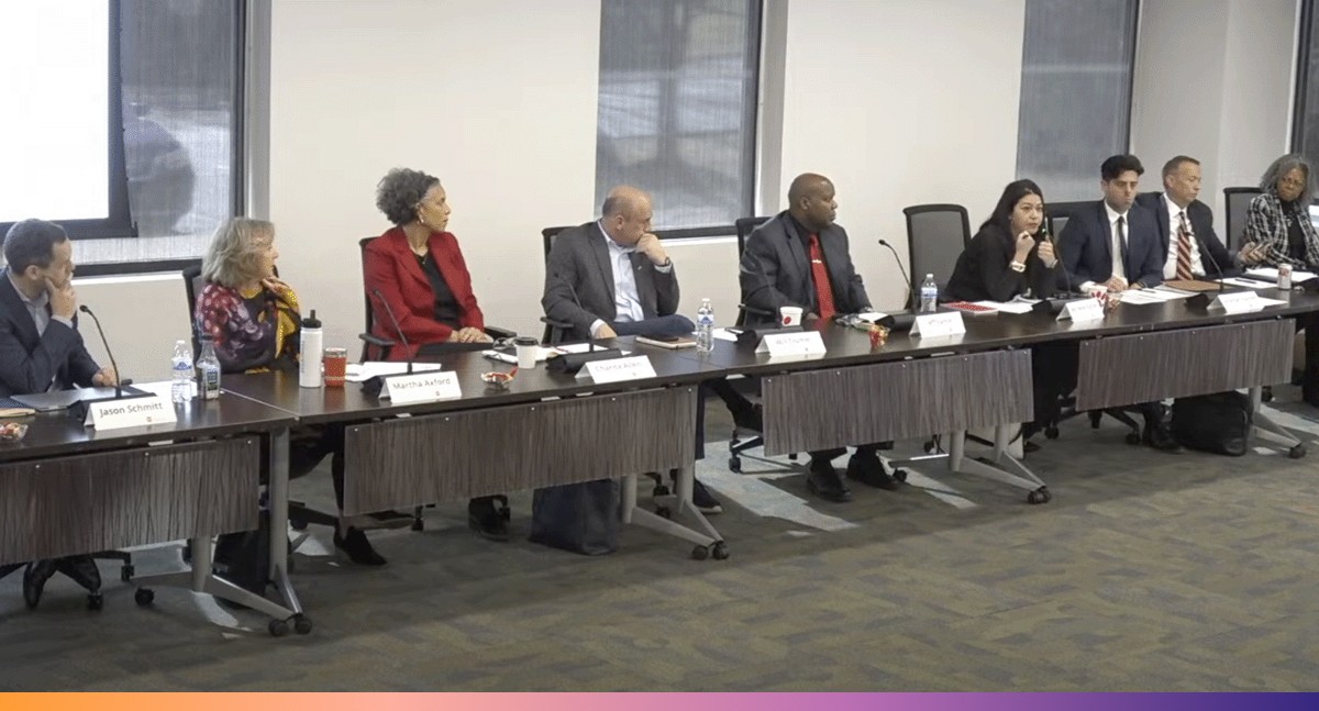 Several businesspeople sit at a long conference table