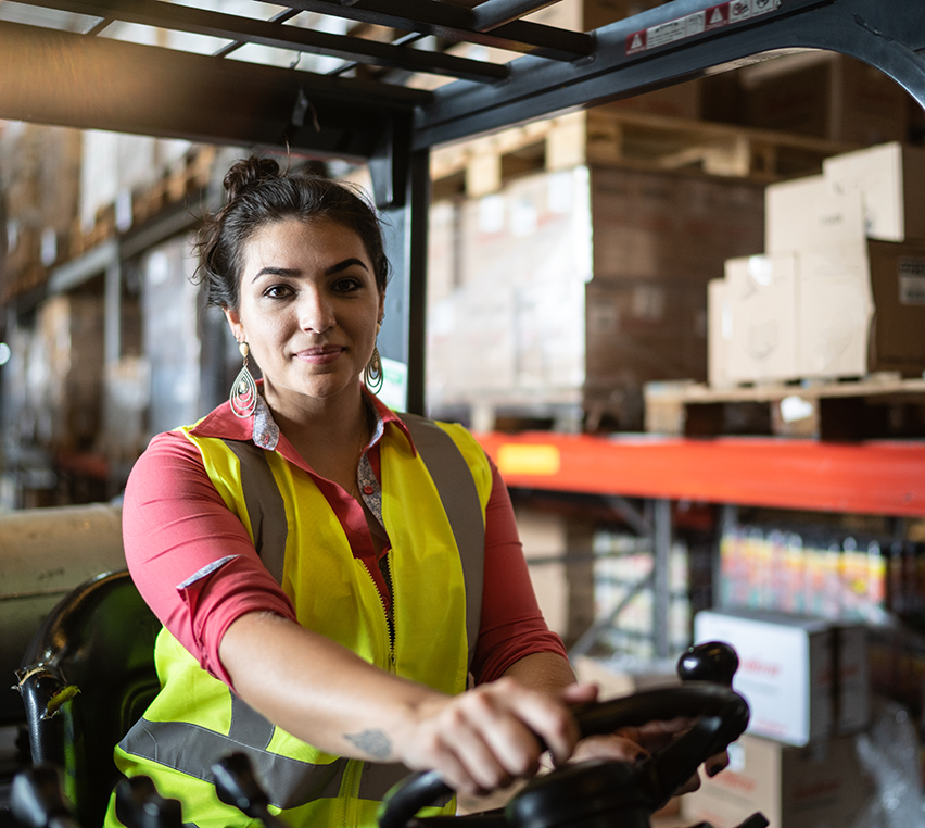 Woman wearing a safety vest drives a forklift