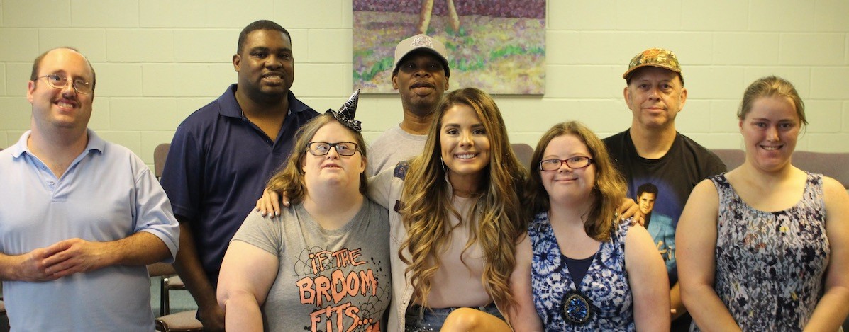 a small group of adults with disabilities of varying ages posing for a group photo and smiling