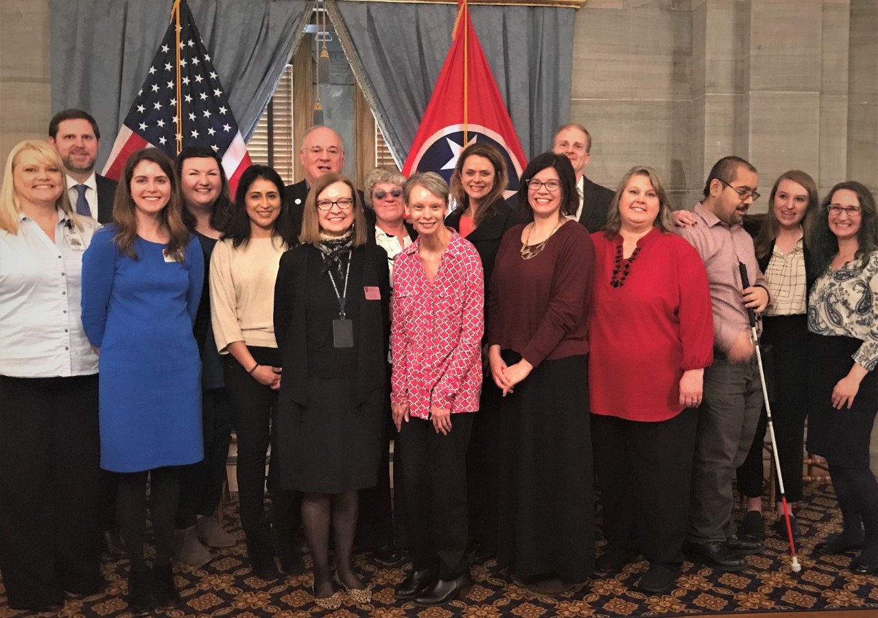 A group of 15 Council members, staff, and two interns are pictured on the stage in the TN Old Supreme Court Chambers after the Disability Policy Alliance program, “State of TN Disability Services”, held during the 2020 Disability Day on the Hill. It is a diverse group of adults with and without disabilities of various ages and ethnicities from across TN. On a later page there is also a photo of Governor Bill Lee speaking at the event at a podium in front of a crowded room