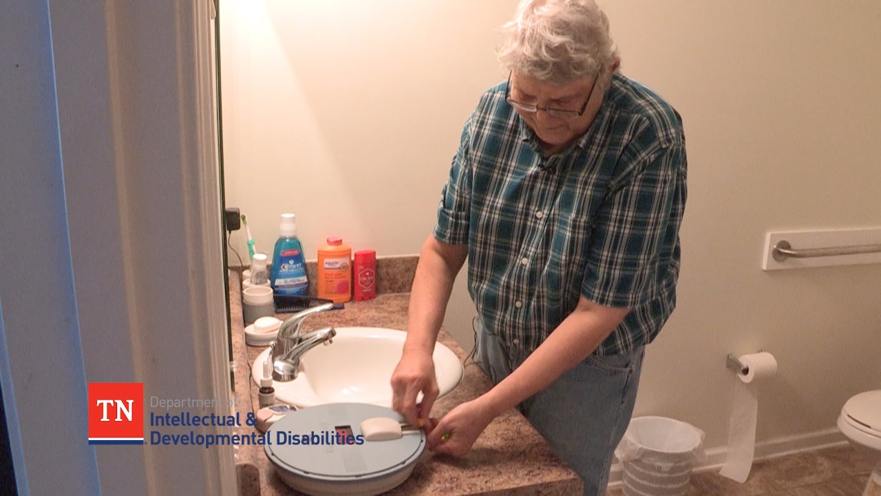 adult man with gray hair is shown in at his bathroom sink in his home, using an automatic medicine dispenser machine