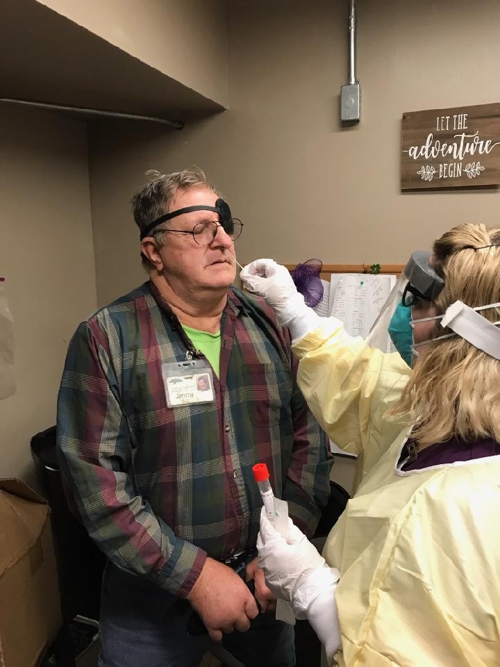 Jimmy, an older gentleman with gray hair and a flannel shirt and an eye patch getting a COVID test via a nose swab from someone in personal protective equipment