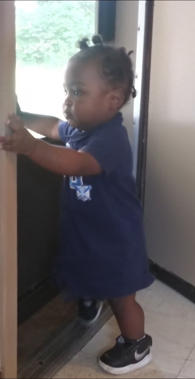 an African-American boy baby or young toddler is standing up, steadying  himself on the wall; he is taking his first steps