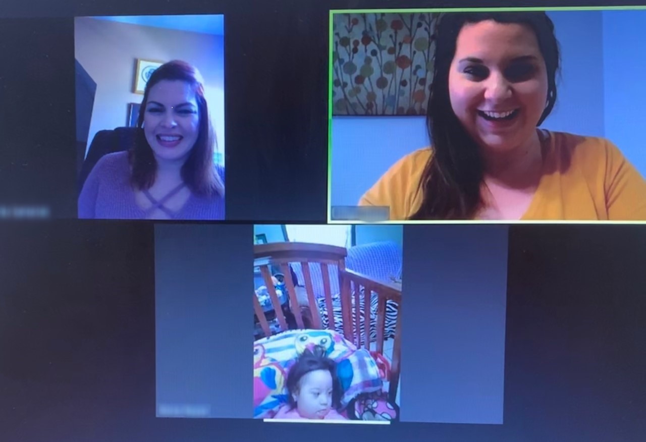 a screenshot of a teletherapy visit; on the screen are two women, the early intervention therapist and the mother of a child getting services, and then an infant laying in her crib is also shown on the video on the computer screen