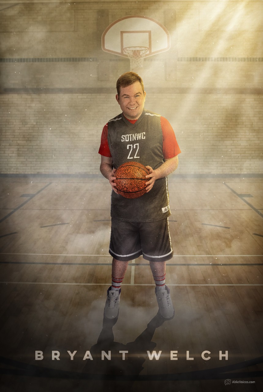 Bryant Welch a young white man with a basketball jersey and athletic shorts and sneakers on, shown on a dim basketball court with a hoop behind him and sunlight streaming into the gyn. He is holding a basketball and has a big smile. His jersey says “SOTNWC” which stands for “Special Olympics TN Williamson County”, and his jersey number is 22