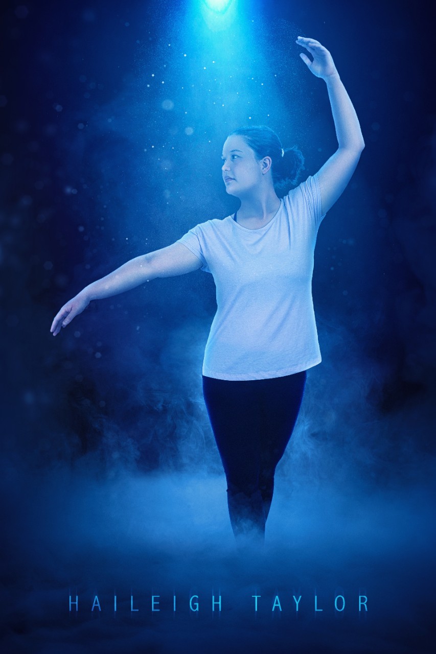 Haileigh Taylor a young white woman in a white t-shirt, black leggings and her brown hair pulled back in a ponytail poses in a dance move with one arm arched gracefully over her head and the other arm out to the side of her body. She’s shown in a blue misty spotlight