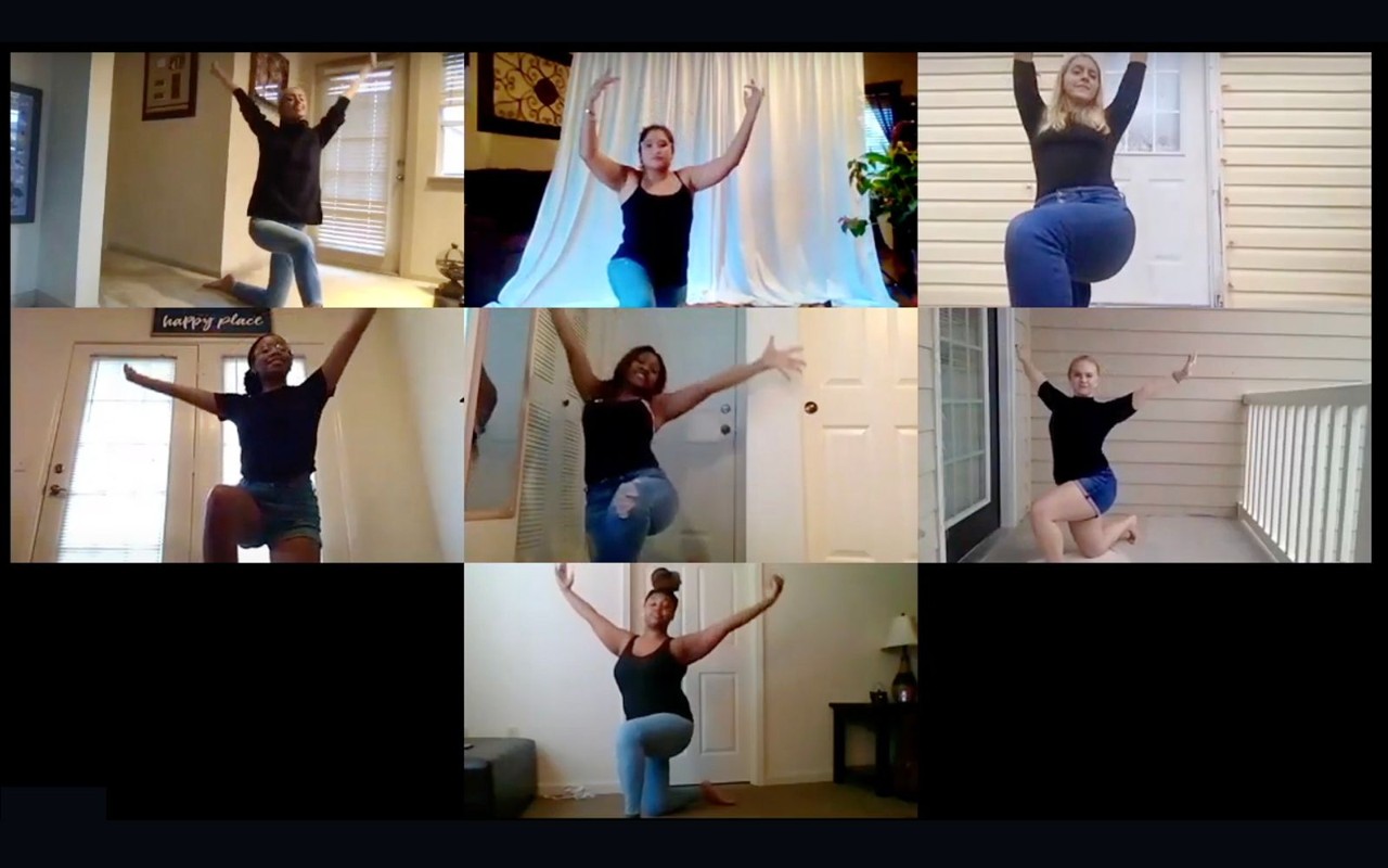 a screenshot of a Zoom or webinar session with 7 young women of varying ages and races doing a similar dance pose with their arms lifted in the air above their head while kneeling on one knee. They are all dressed alike in black shirts and jeans. They are doing a dance lesson together virtually