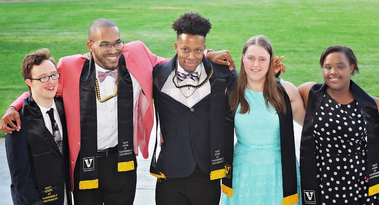 Next Steps at Vanderbilt and shows 5 students on their graduation day, dressed in formal clothes and wearing academic sashes with the Vanderbilt logo around their necks. There are three young Black men, one young white woman, one young Black woman and one young white man. Two of the grads have Down syndrome.