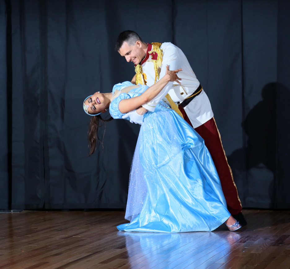  a woman dressed in a blue dress like Disney’s “Cinderella” and a man dipping her back in a dance move, dressed as Prince Charming from Cinderella.