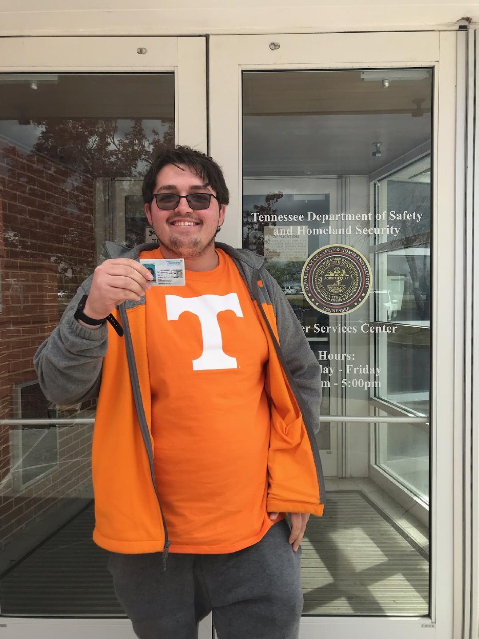 young white man with brown hair wearing an orange University of TN and jacket, holding up his student ID