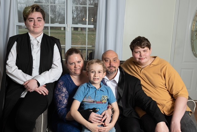 family photo of 2 adults, who are blind, and 3 children of varying ages seated together on a couch in a living room
