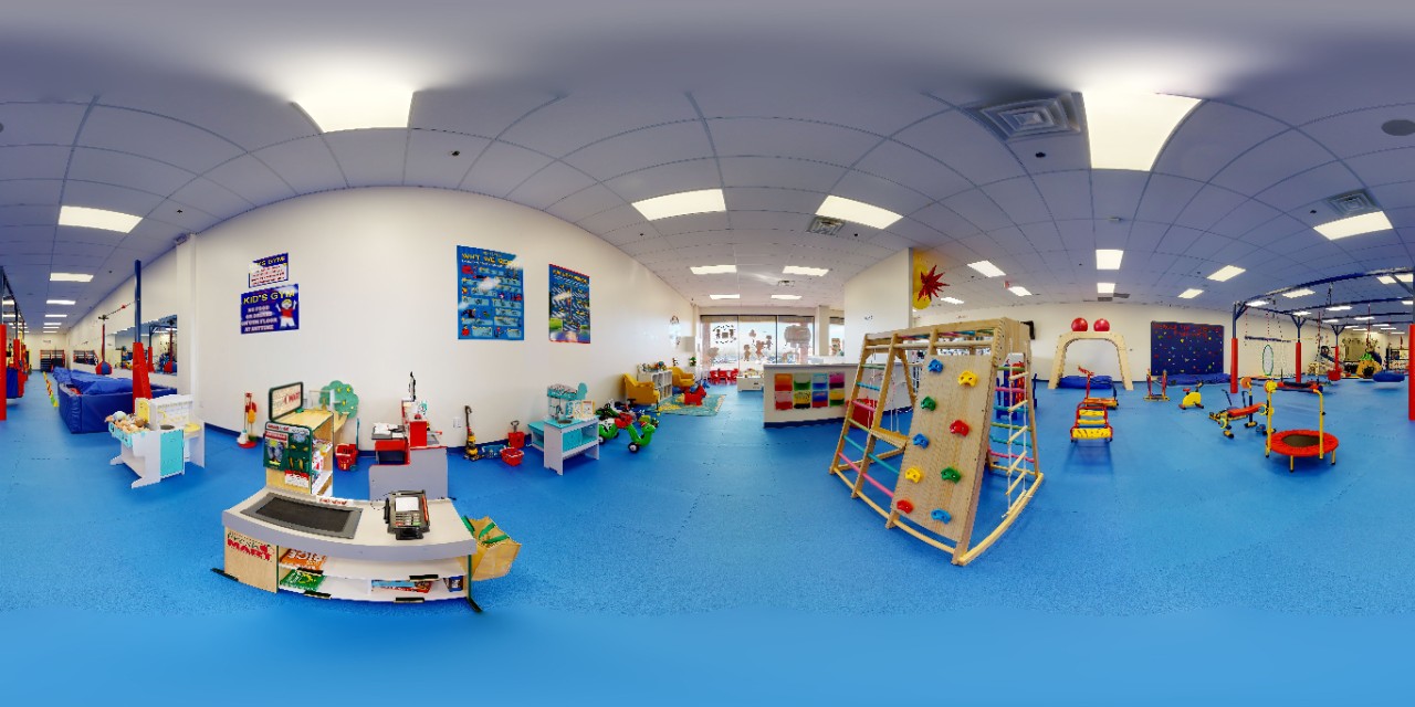 fish-eye lens photo showing brightly colored sensory-friendly play and gym equipment in a large gym space covered with safety mats on the floor