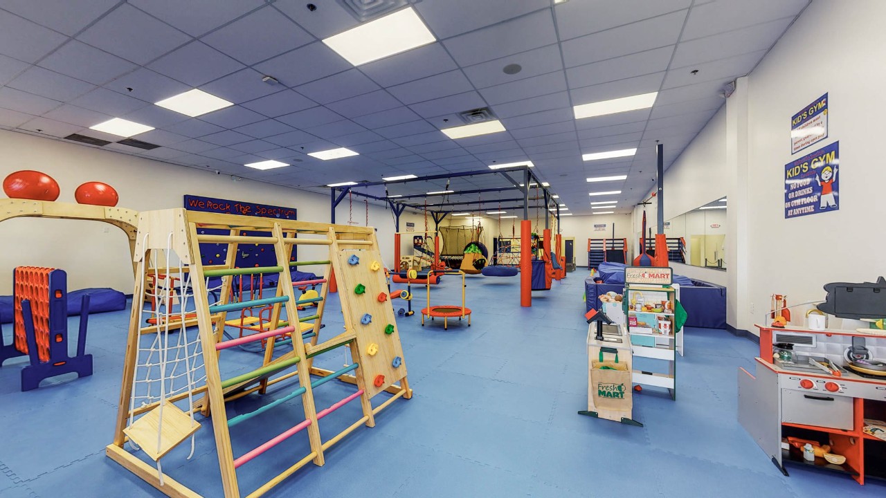 brightly colored sensory-friendly play and gym equipment in a large gym space covered with safety mats on the floor