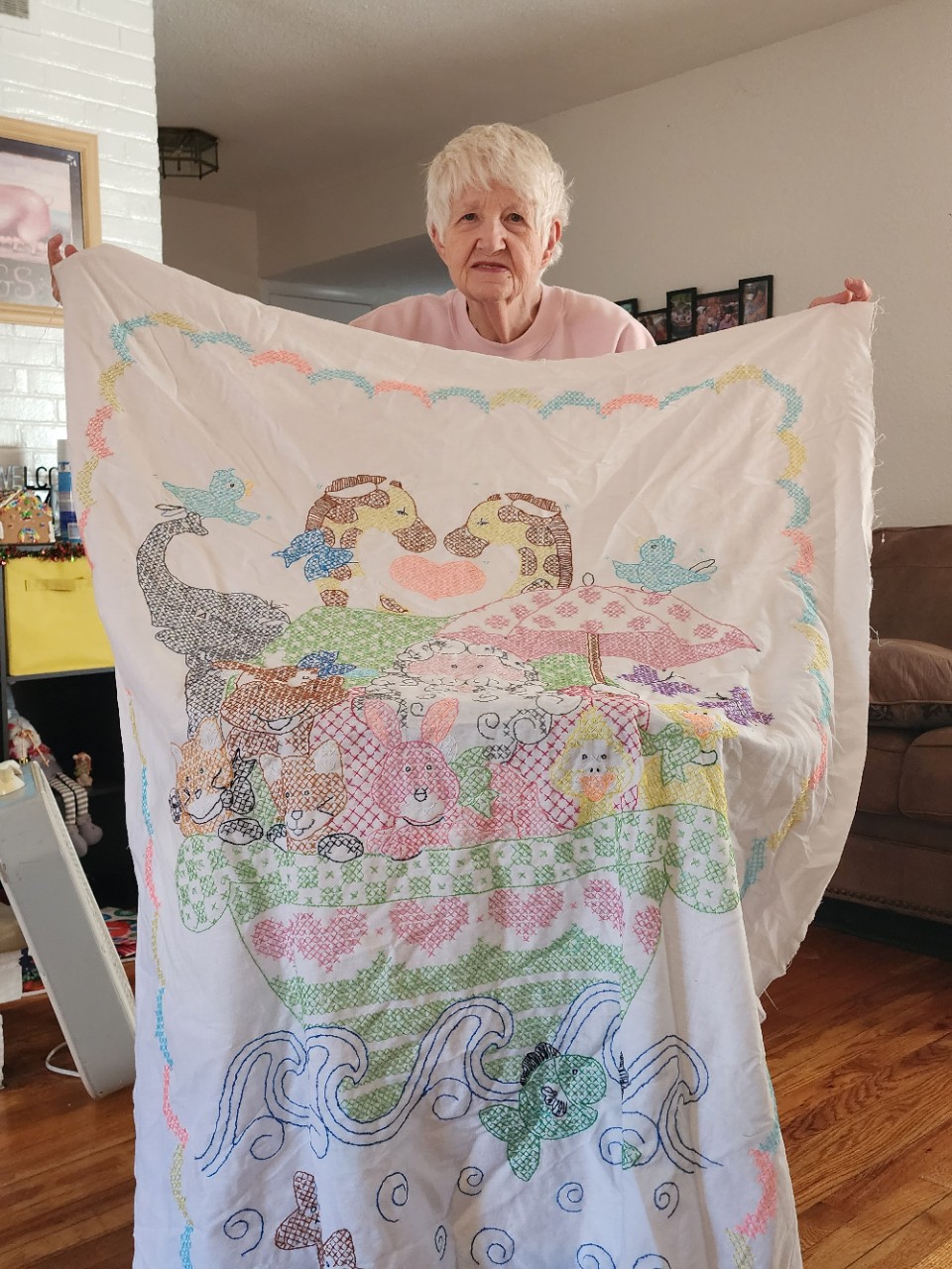 an intricately sewn blanket with a white background and all sorts of animals in pastel colors; it appears to be a scene of Noah's ark with pairs of animals in a boat on the water